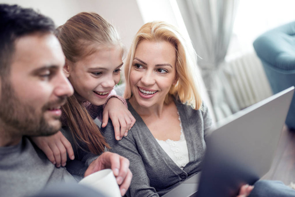 Família jovem olhando para o laptop juntos em casa
. - Foto, Imagem