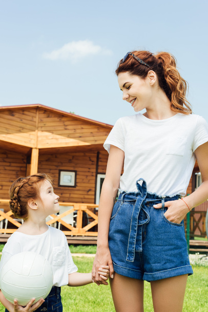 mother and daughter with volleyball ball in white t-shirts in front of wooden cottage - Photo, Image