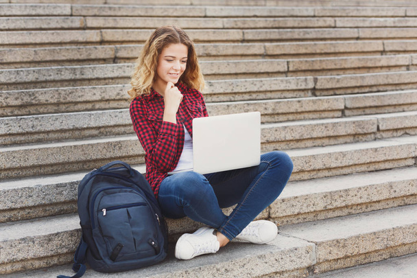 ノート パソコンを屋外で使う階段に座っている学生少女の笑みを浮かべてください。 - 写真・画像