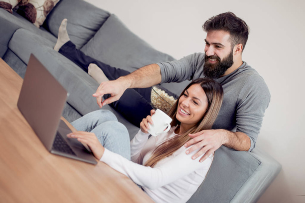 Jovem casal feliz sentado em um sofá e trabalhando juntos em casa
. - Foto, Imagem