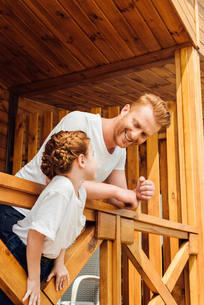 Gelukkig vader en dochter samen tijd doorbrengen op terras van houten huisje - Foto, afbeelding