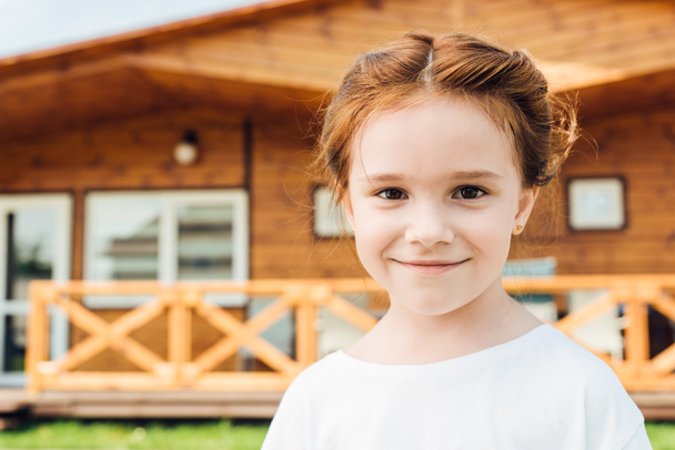 happy little child looking at camera in front of wooden cottage - Photo, Image