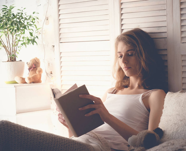 lifestyle and people concept:Young blond woman lying in bed while reading a book - Fotó, kép