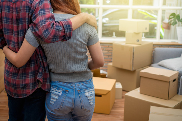 Back side of Asian young couple hugging together over the big cardboard box and sofa when moving in new house, Moving and House Hunting concept - Photo, Image