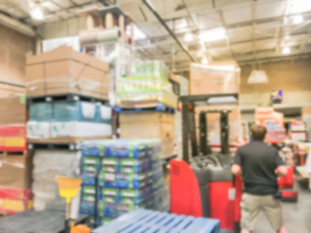 Blurred large warehouse with working forklift stacking unloading goods. Defocused industrial distribution interior row aisles, shelves from floor to ceiling in America. Inventory, wholesale concept - Photo, Image