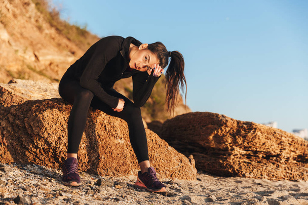 Tired sportswoman sitting at the beach after jogging - Foto, Bild