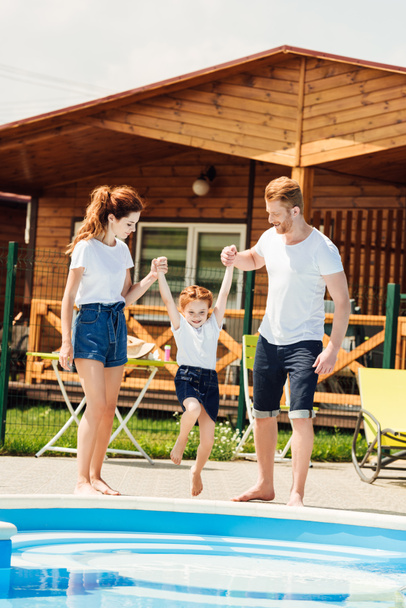 beautiful young family playing at poolside of cozy wooden cottage - Фото, зображення