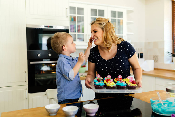 Criança bonito grato à mãe enquanto prepara biscoitos na cozinha
 - Foto, Imagem