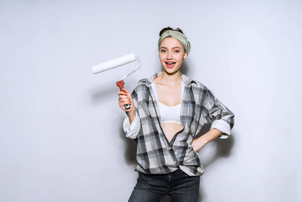 funny young girl in plaid shirt colors the walls in white with a roller, repair in the apartment - Zdjęcie, obraz