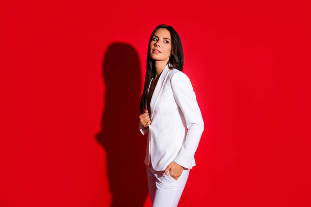 Side view portrait of gorgeous charming woman in white suit holding hand in pocket looking away isolated on bright red background - Valokuva, kuva