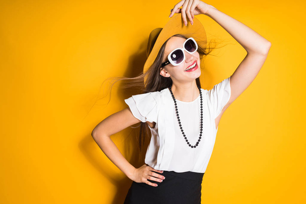 luxurious beautiful long-haired girl model in hat and sunglasses posing on orange background - Fotó, kép