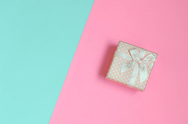Маленька рожева подарункова коробка лежить на текстурі модного пастельного синього та рожевого кольорів паперу в мінімальній концепції
. - Фото, зображення