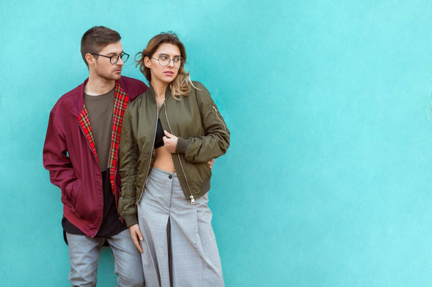 fashion couple in their glasses with burgundy clothes posing on a blue wooden wall - Zdjęcie, obraz