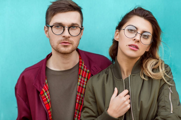fashion couple in their glasses with burgundy clothes posing on a blue wooden wall - Foto, Bild