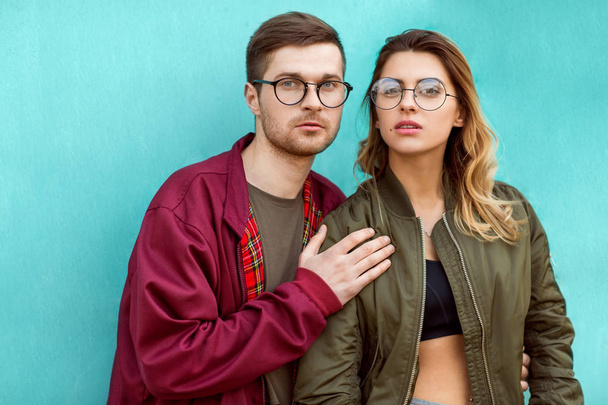 fashion couple in their glasses with burgundy clothes posing on a blue wooden wall - Fotoğraf, Görsel
