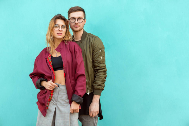 fashion couple in their glasses with burgundy clothes posing on a blue wooden wall - Foto, imagen