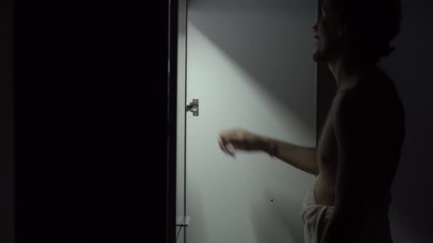 Young man at night opens the wardrobe and chooses the shirt to wear - Materiał filmowy, wideo