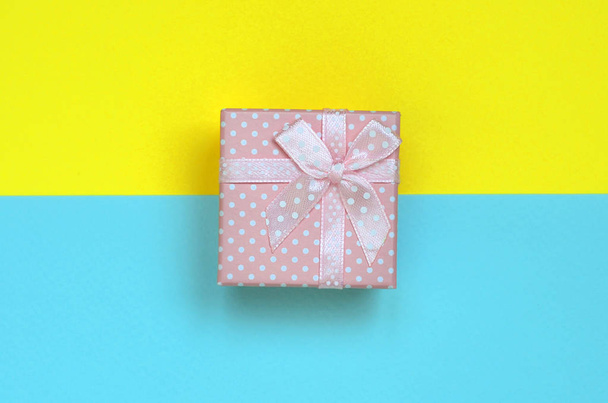 Small pink gift box lie on texture background of fashion pastel blue and yellow colors paper in minimal concept. - Fotó, kép