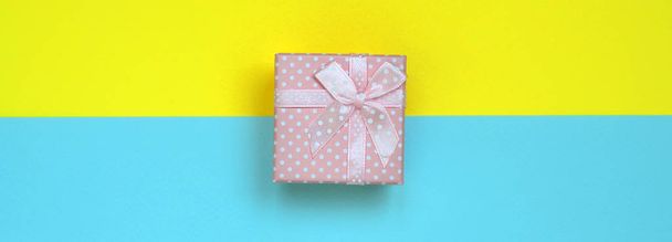 Kleine roze geschenk doos leugen op textuur achtergrond van mode pastel blauw en geel kleuren papier in minimale concept. - Foto, afbeelding