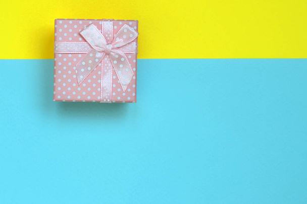 Pequena caixa de presente rosa encontra-se no fundo textura da moda pastel azul e amarelo cores papel no conceito mínimo
. - Foto, Imagem