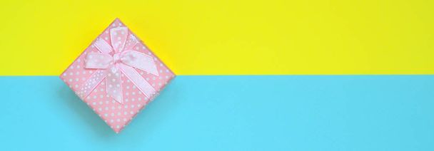 Маленькая розовая коробка подарка лежат на фоне текстуры моды пастельно-синий и желтый цвета бумаги в минимальной концепции
. - Фото, изображение