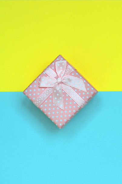 Small pink gift box lie on texture background of fashion pastel blue and yellow colors paper in minimal concept. - Фото, изображение