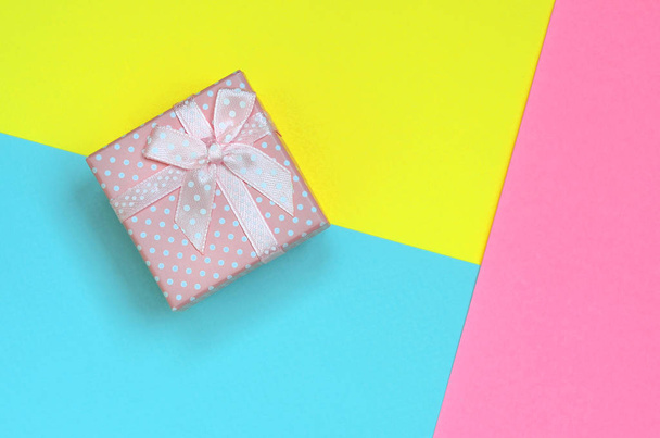 Маленькая розовая коробка подарка лежат на фоне текстуры моды пастель синий, желтый и розовый цвета бумаги в минимальной концепции
. - Фото, изображение