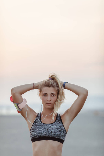 Bonita esportista caucasiana em pé na praia e olhando para a câmera
. - Foto, Imagem