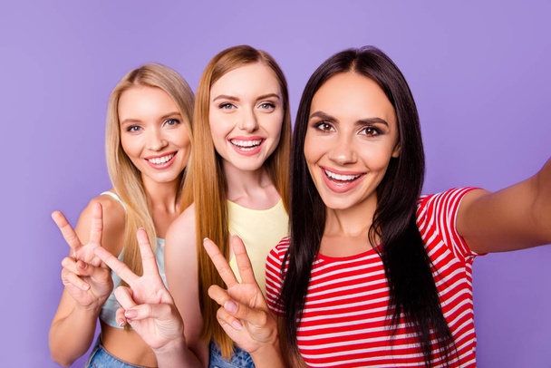 Self portrait of pretty attractive girls gesturing v-signs shooting selfie on front camera isolated on bright violet background. Photography concept - Foto, immagini