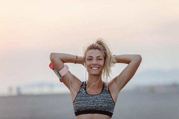 Pretty Caucasian smiling sportswoman standing on beach and looking at camera. - 写真・画像