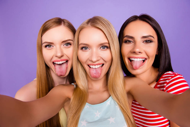 Self portrait of funky childish trio gesturing tongues out shooting selfie on front camera having leisure isolated on bright violet background. Rest relax leisure concept - Foto, afbeelding