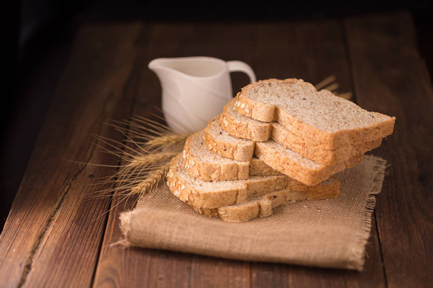 Нарезанный хлеб из цельной пшеницы на деревянном столе с кружкой молока
 - Фото, изображение