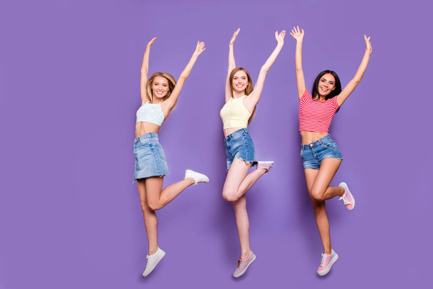 Portrait of cheerful positive trio with thin raised legs jumping in air holding arms up looking at camera isolated on bright violet background. Holiday vacation weekend concept - Foto, Bild