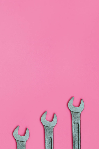 Three metallic spanners lie on texture background of fashion pastel pink color paper in minimal concept. - Фото, изображение