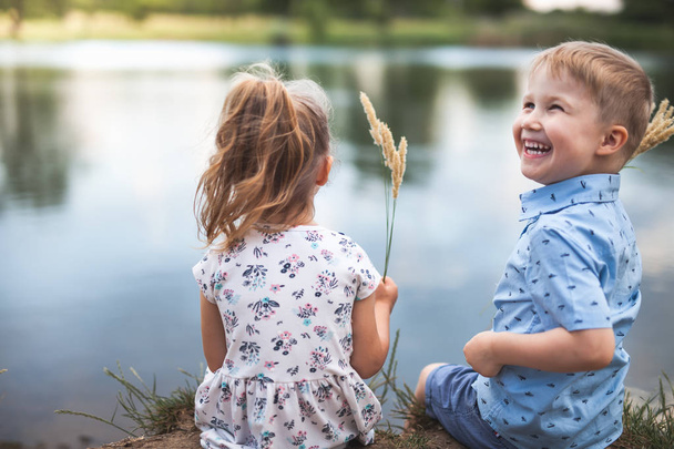 Your Happy Kids, Girl And Boy Are Sitting Near Lake - Fotografie, Obrázek