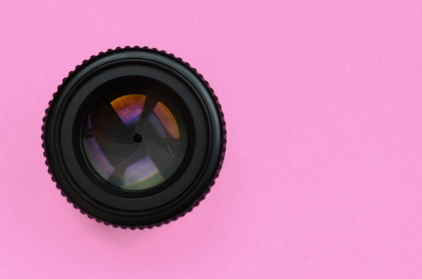 Camera lens with a closed aperture lie on texture background of fashion pastel pink color paper in minimal concept. - Photo, Image