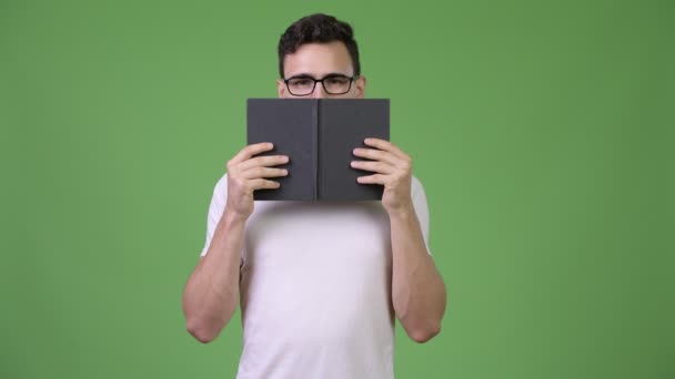 Young handsome nerd man covering face with book - Metraje, vídeo