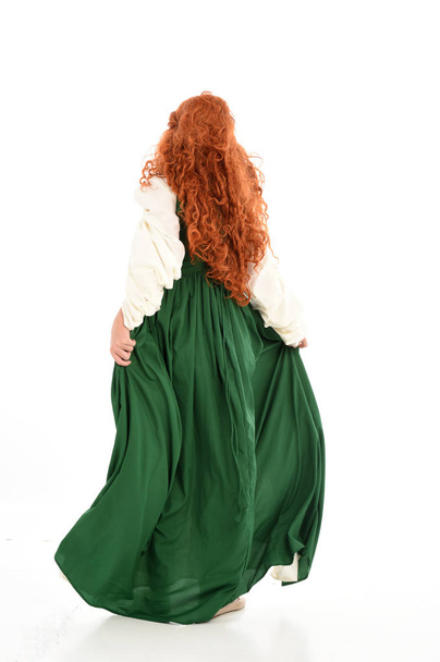 full length portrait of red haired girl wearing green medieval gown. standing pose on white studio background. - Photo, Image
