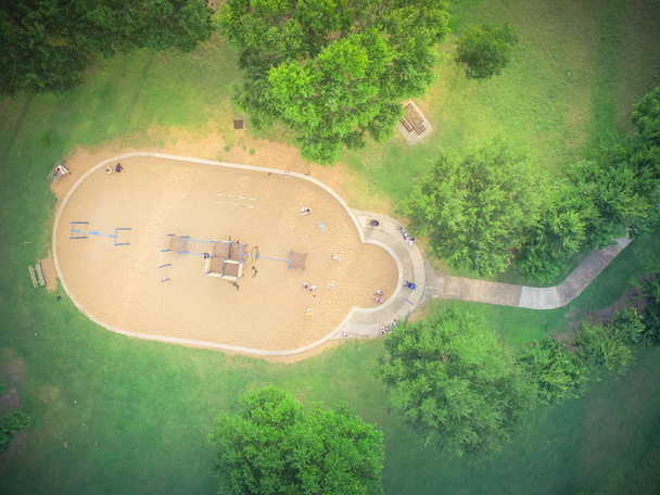 Aerial view of a big kid games playground at Harwin Park in Houston, Texas. An elevated view of slides and swings in the park surrounded by green trees. Children outdoor play and recreation concept. - Photo, Image