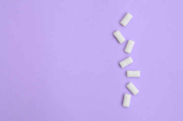 A few chewing gums lie on texture background of fashion pastel violet color paper in minimal concept. - Foto, afbeelding