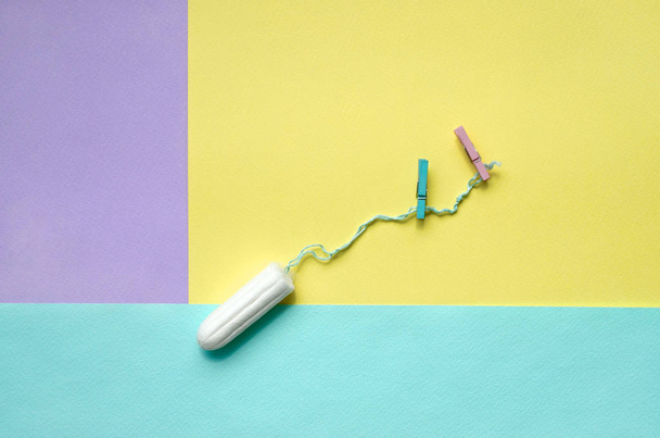 Tampon with two clothespins lie on texture background of fashion pastel violet, yellow and blue colors paper in minimal concept. - Фото, изображение