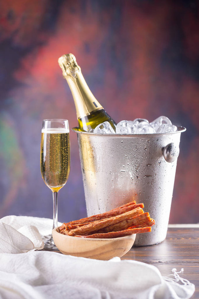 Champagne bottle in bucket with ice and glass of champagne on dark background. - Photo, Image