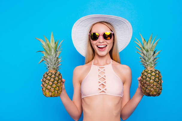 Portrait of positive funky girl in eyeglasses having two pineapples in hands looking at camera isolated on vivid blue background. Exotic concept - Foto, Imagen
