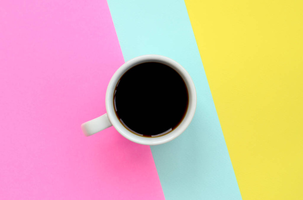 Pequeña taza de café blanco en el fondo de textura de la moda pastel azul, amarillo y rosa colores papel en concepto mínimo
. - Foto, Imagen