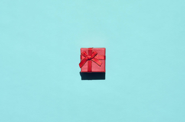 Small red pink gift box lie on texture background of fashion trendy pastel blue color paper in minimal concept. - Photo, Image