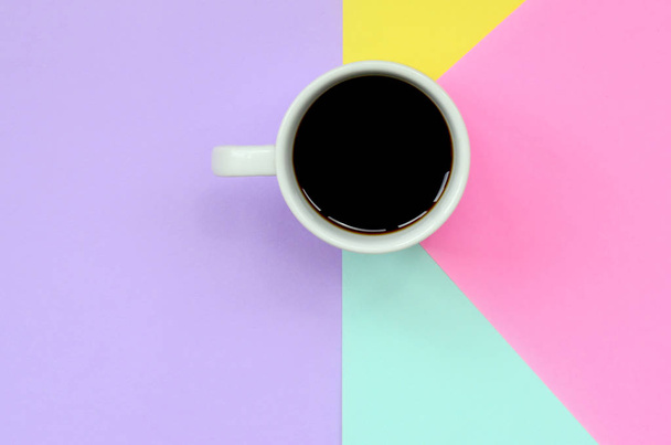 Small white coffee cup on texture background of fashion pastel blue, yellow, violet and pink colors paper in minimal concept. - Photo, Image
