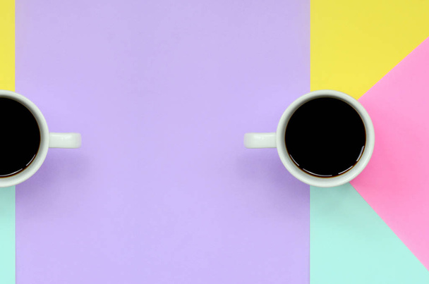 Due piccole tazze di caffè bianco su sfondo texture di carta di colori blu pastello, giallo, viola e rosa moda nel concetto minimale
. - Foto, immagini