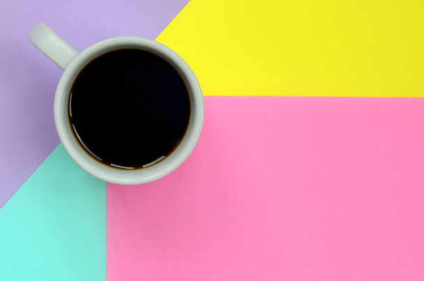 Pequeña taza de café blanco en el fondo de textura de la moda pastel azul, amarillo, violeta y rosa colores papel en concepto mínimo
. - Foto, imagen