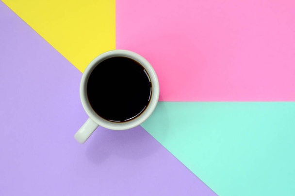 Small white coffee cup on texture background of fashion pastel blue, yellow, violet and pink colors paper in minimal concept. - Photo, Image