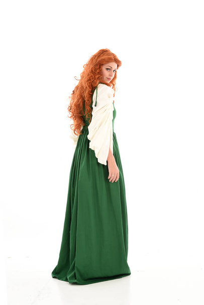 中世のグリーンのドレスを身に着けている赤髪の女の子の完全な長さの肖像画。ホワイト スタジオの背景に立ちポーズ. - 写真・画像
